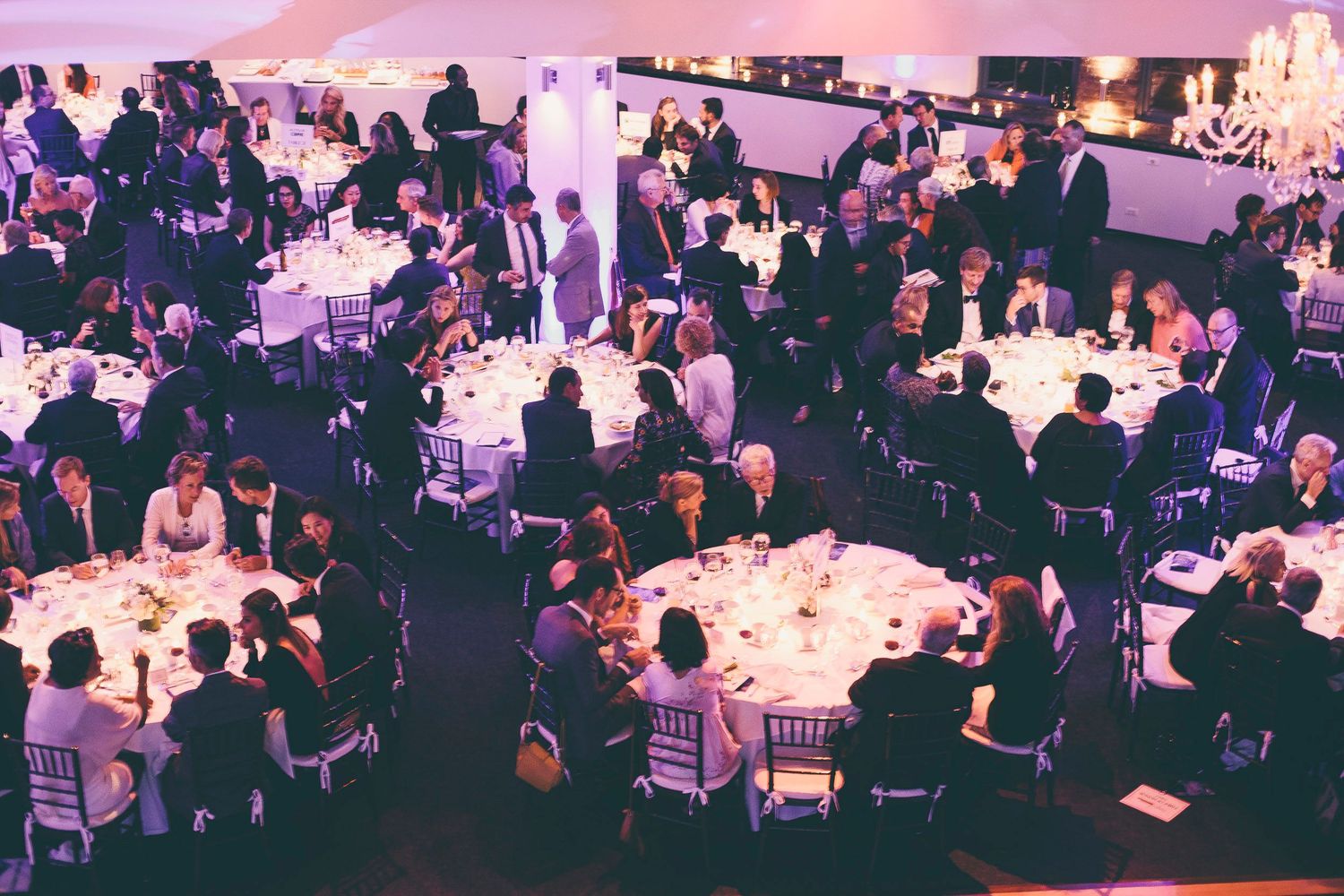 Elegant gala dinner event with guests seated at round tables in white venue.