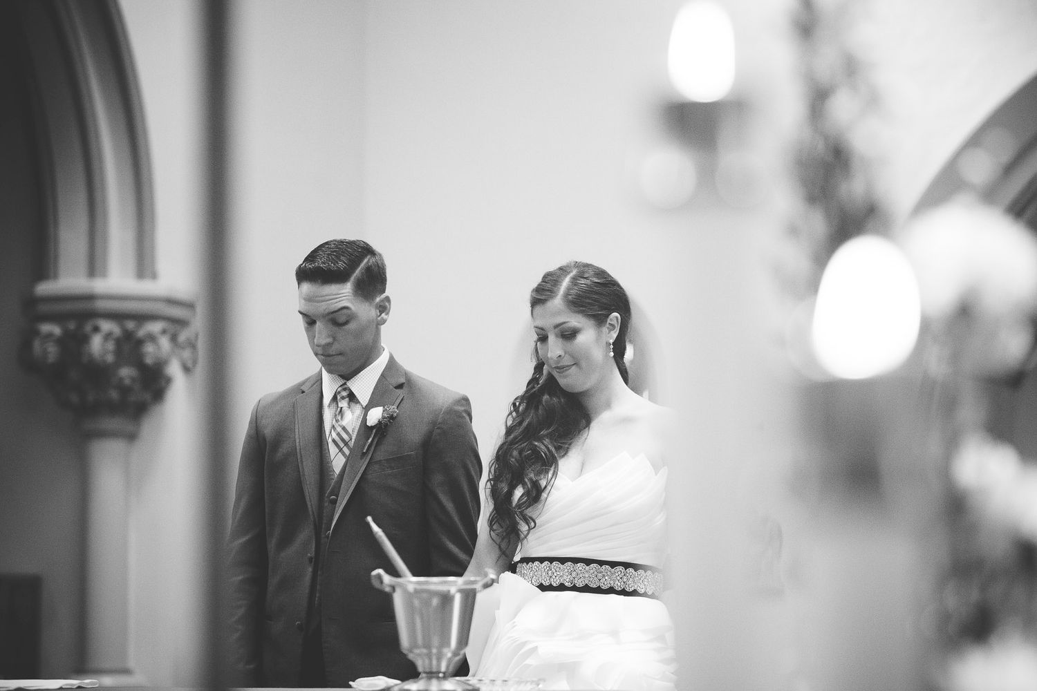 Bride and groom bowing their heads in prayer during their black and white wedding ceremony at the altar.