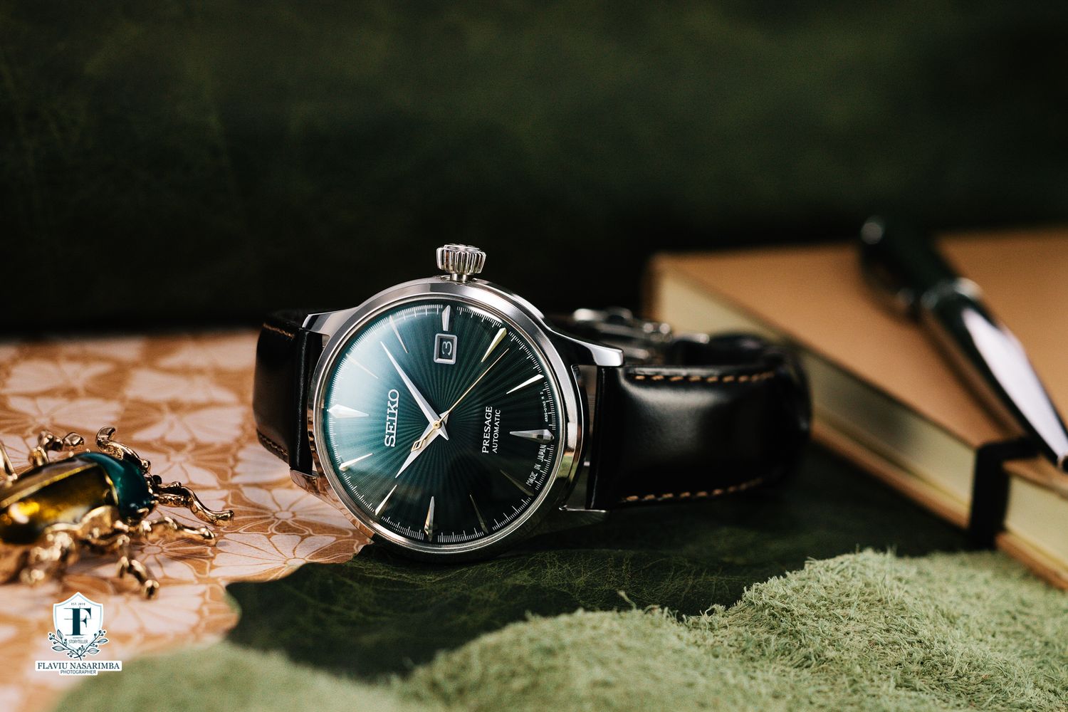 Tissot automatic watch with green sunburst dial on black leather strap beside a notebook.