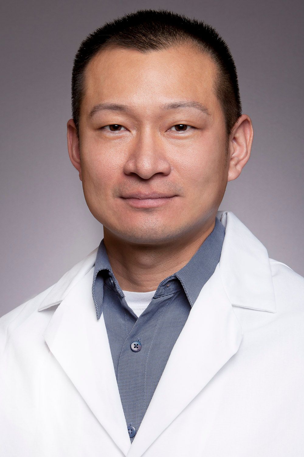 Asian male doctor in white lab coat smiling for a professional medical headshot portrait.