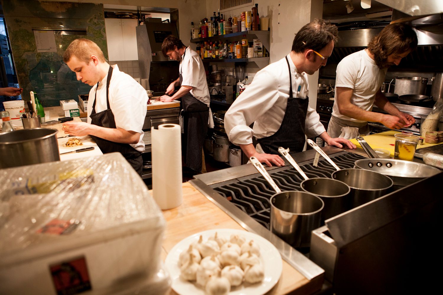 Chefs in black aprons cooking and preparing food in a busy professional restaurant kitchen.