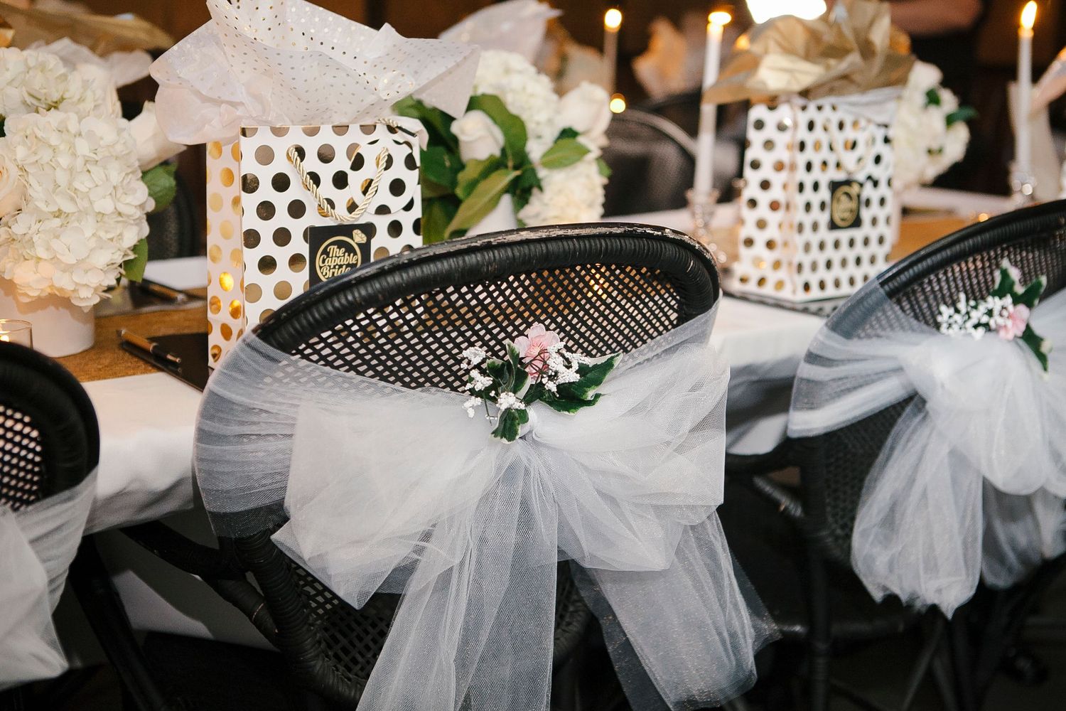 Black chairs elegantly decorated with white tulle bows and floral accents at a wedding planning event.