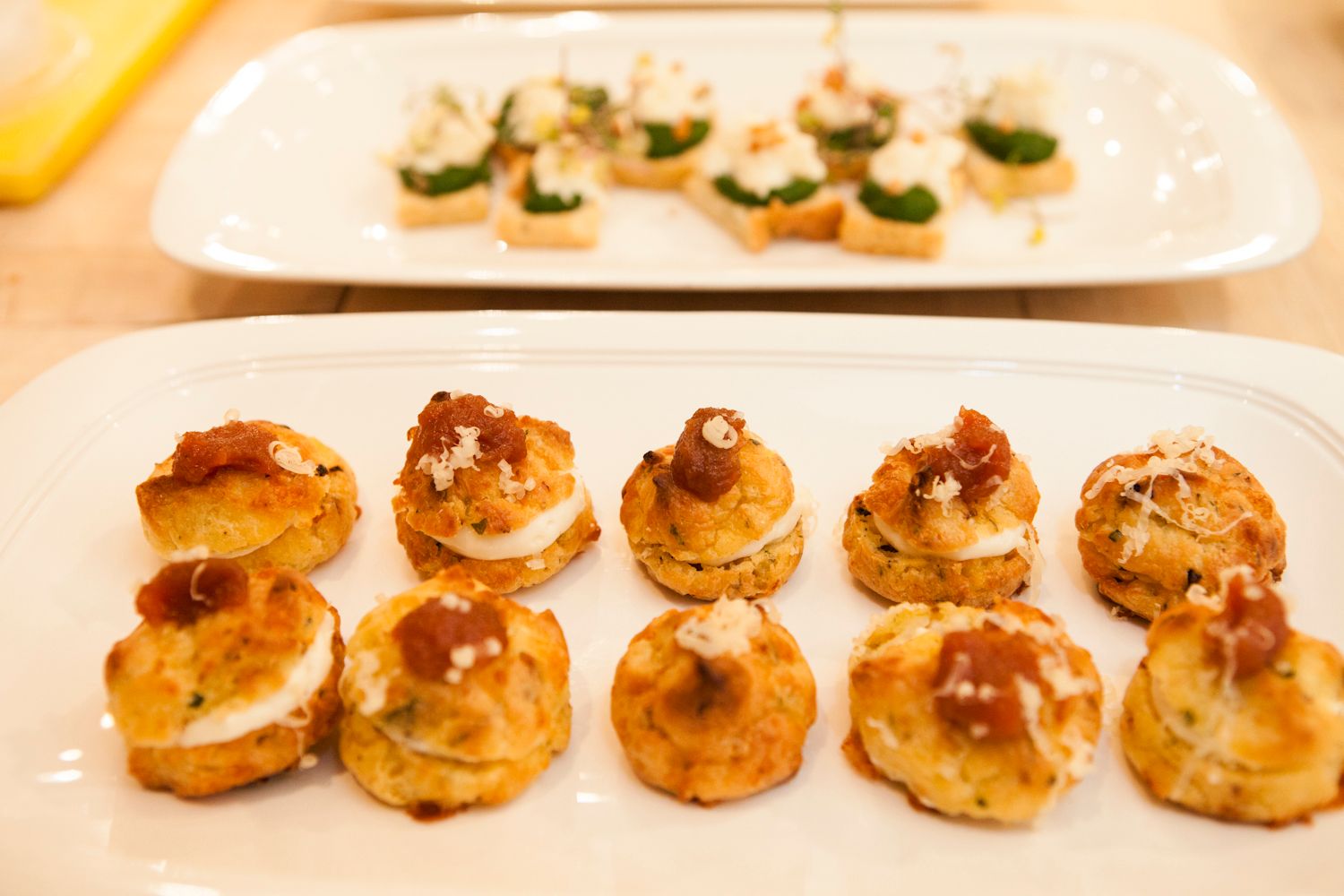 Savory mini cream puff pastries with toppings on white plate with herb crostini behind.