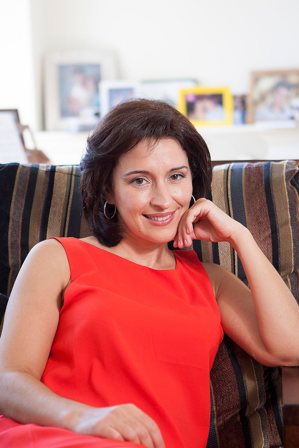 Happy brunette woman in red dress relaxing on striped sofa at home.