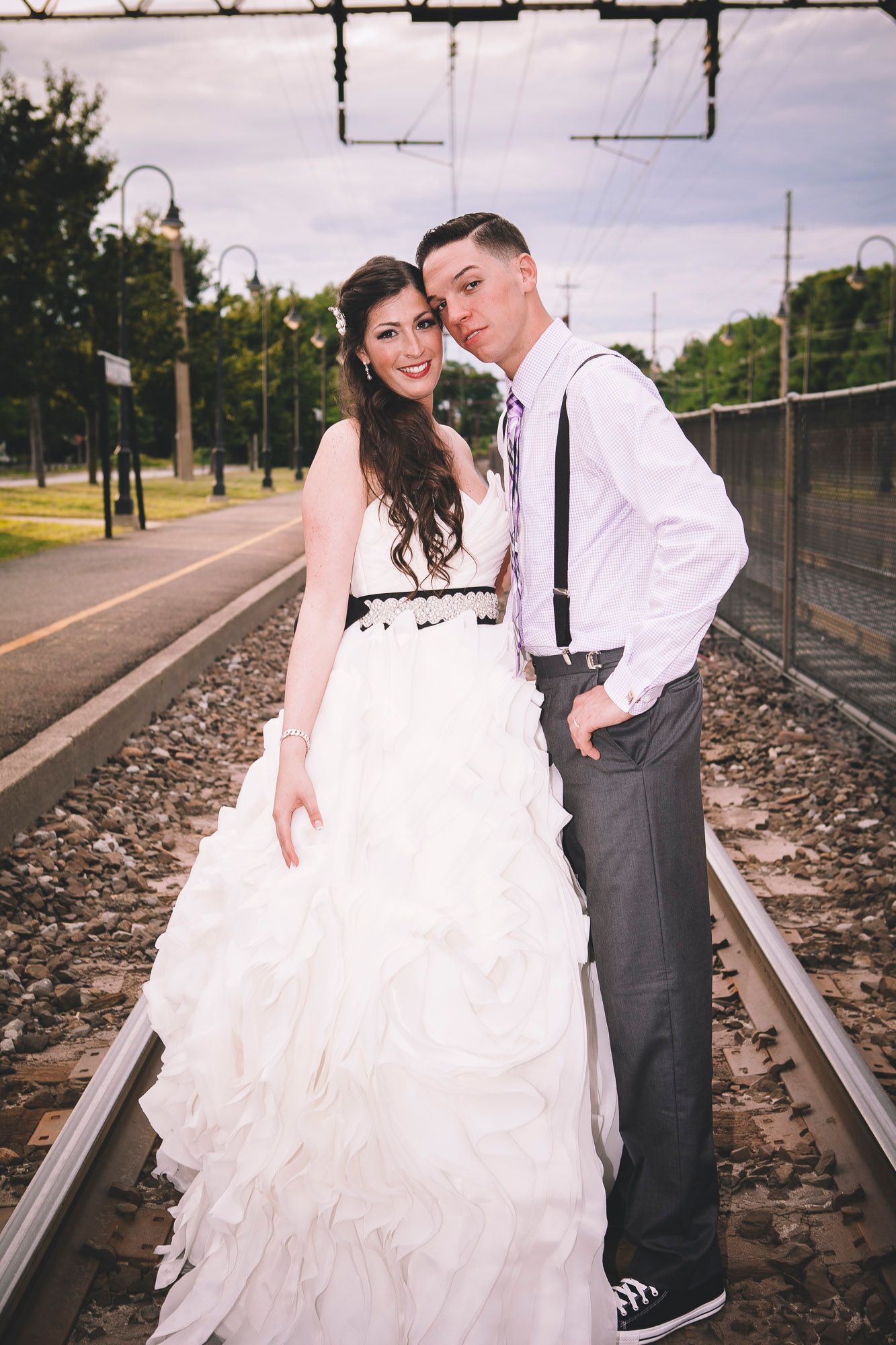 Smiling bride and groom posing together on railroad tracks in wedding attire on their wedding day.