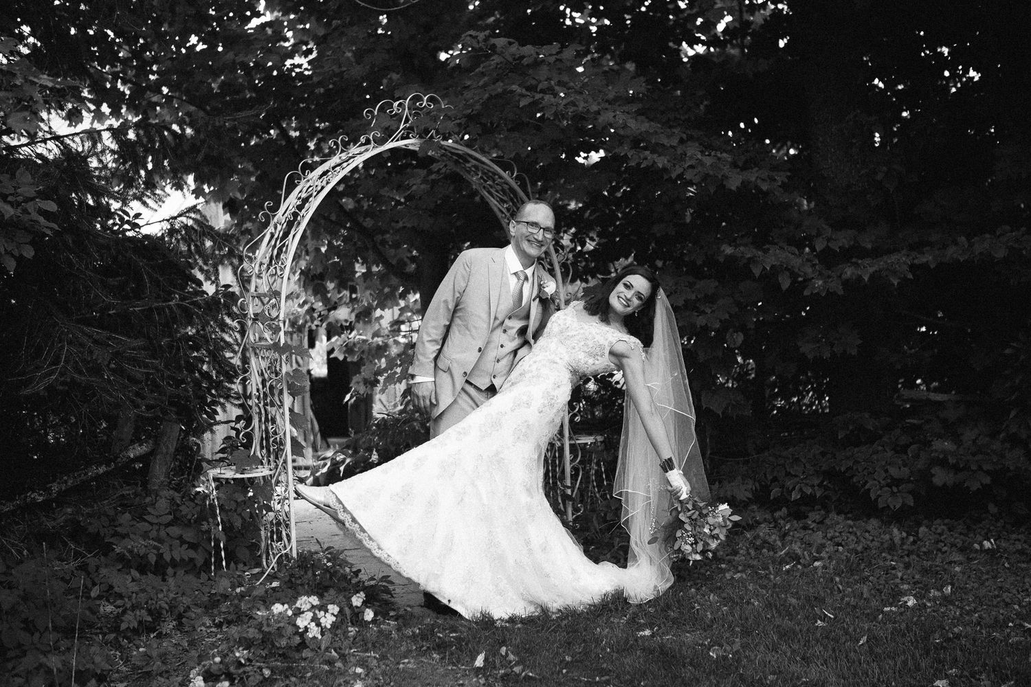 Black and white photo of groom dipping bride dramatically under a decorative iron garden arch.