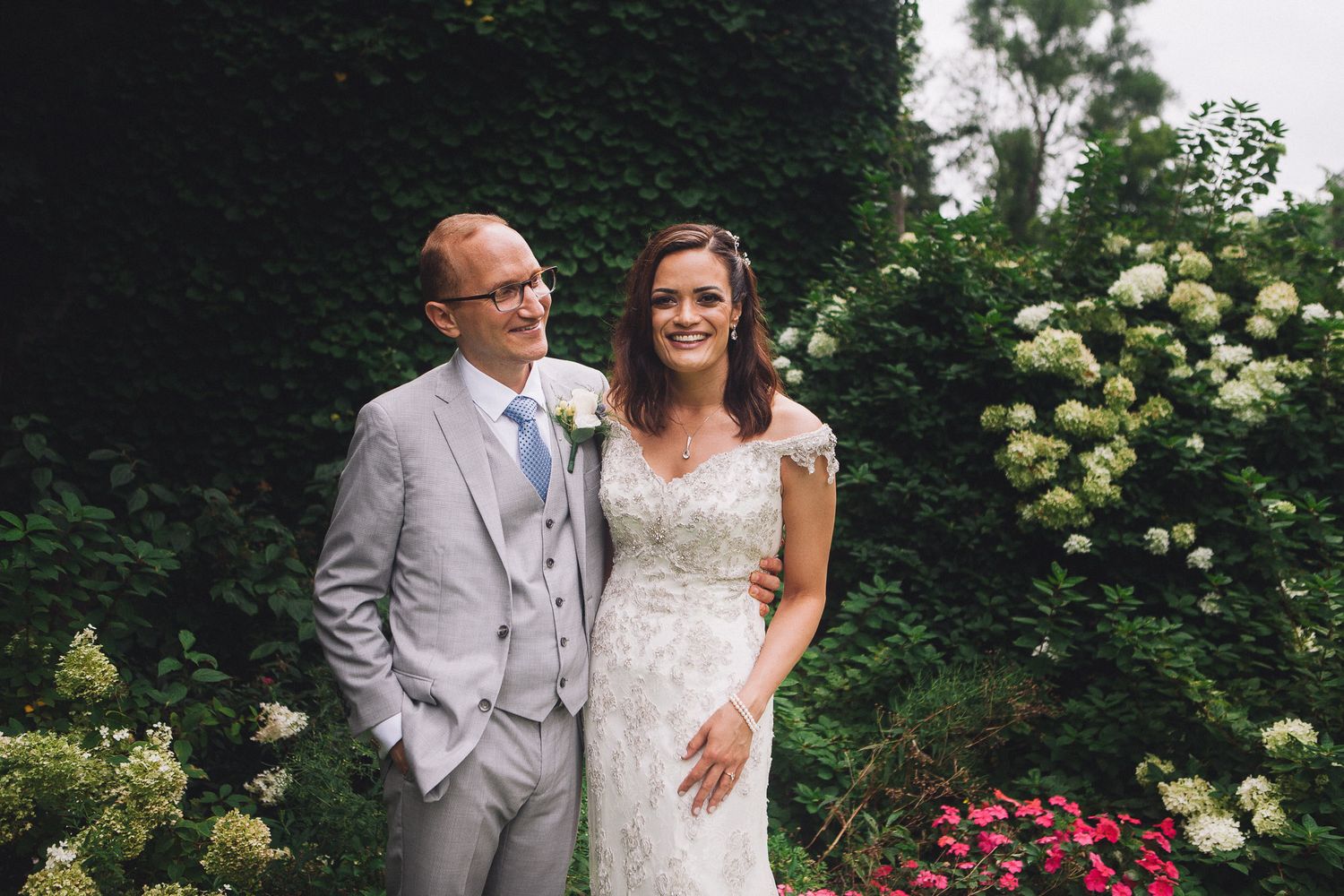 Bride and groom smiling together among white hydrangeas in garden wedding portrait.