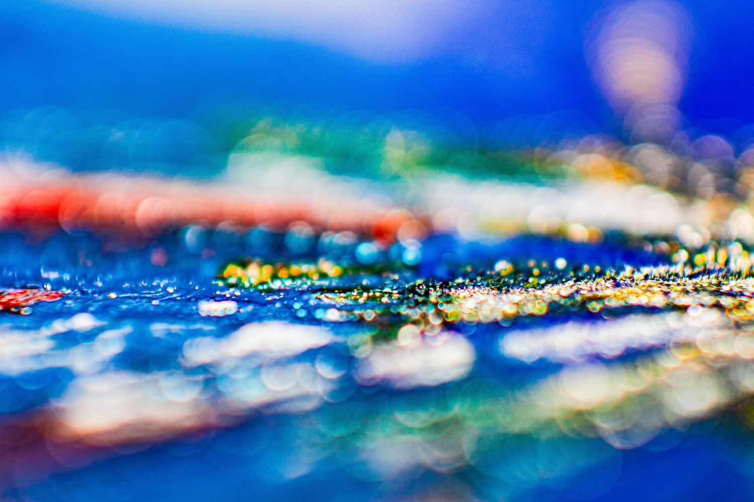 Abstract macro photography of colorful bokeh lights reflecting on a wet blue surface with glittering details.