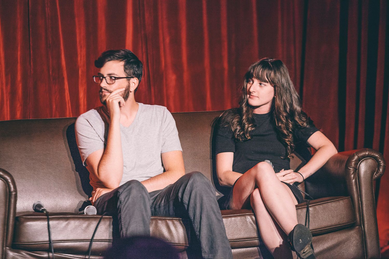 Man and woman seated on leather couch on stage during panel discussion event.