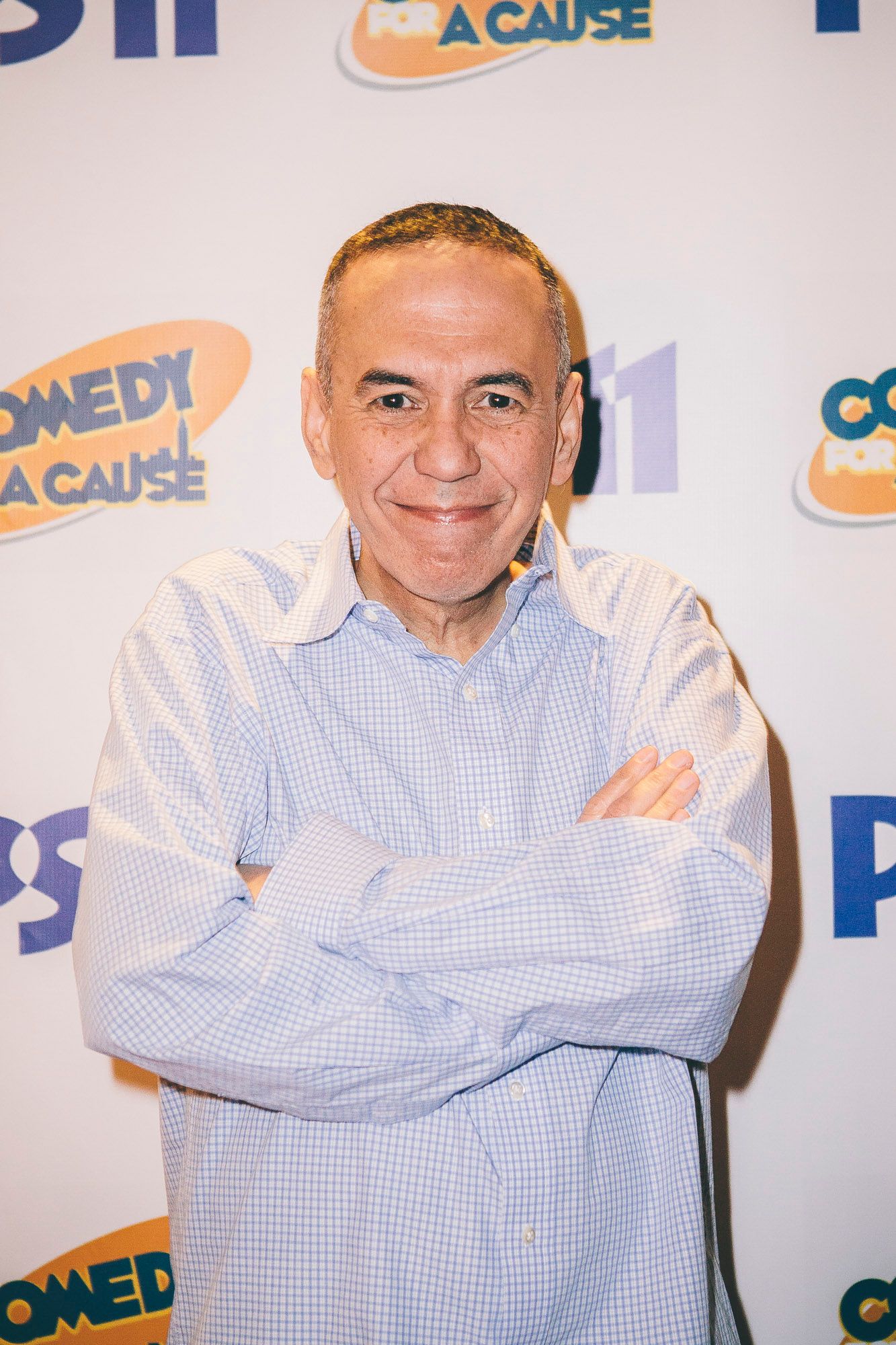 Smiling man with arms crossed posing at PS11 Comedy for a Cause charity event backdrop.