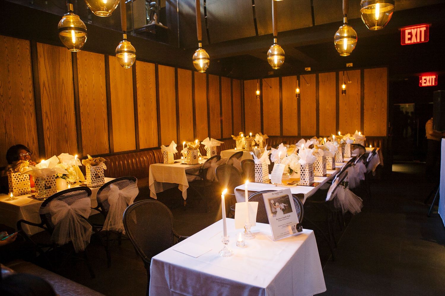 Intimate restaurant event space with gold pendant lights, white tablecloths, and candles creating a warm ambiance.