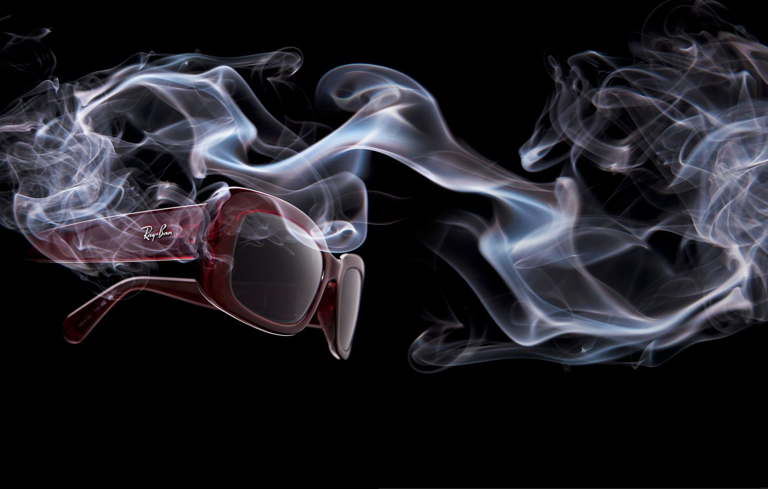 Artistic photograph of red sunglasses surrounded by swirling white smoke on a black background.