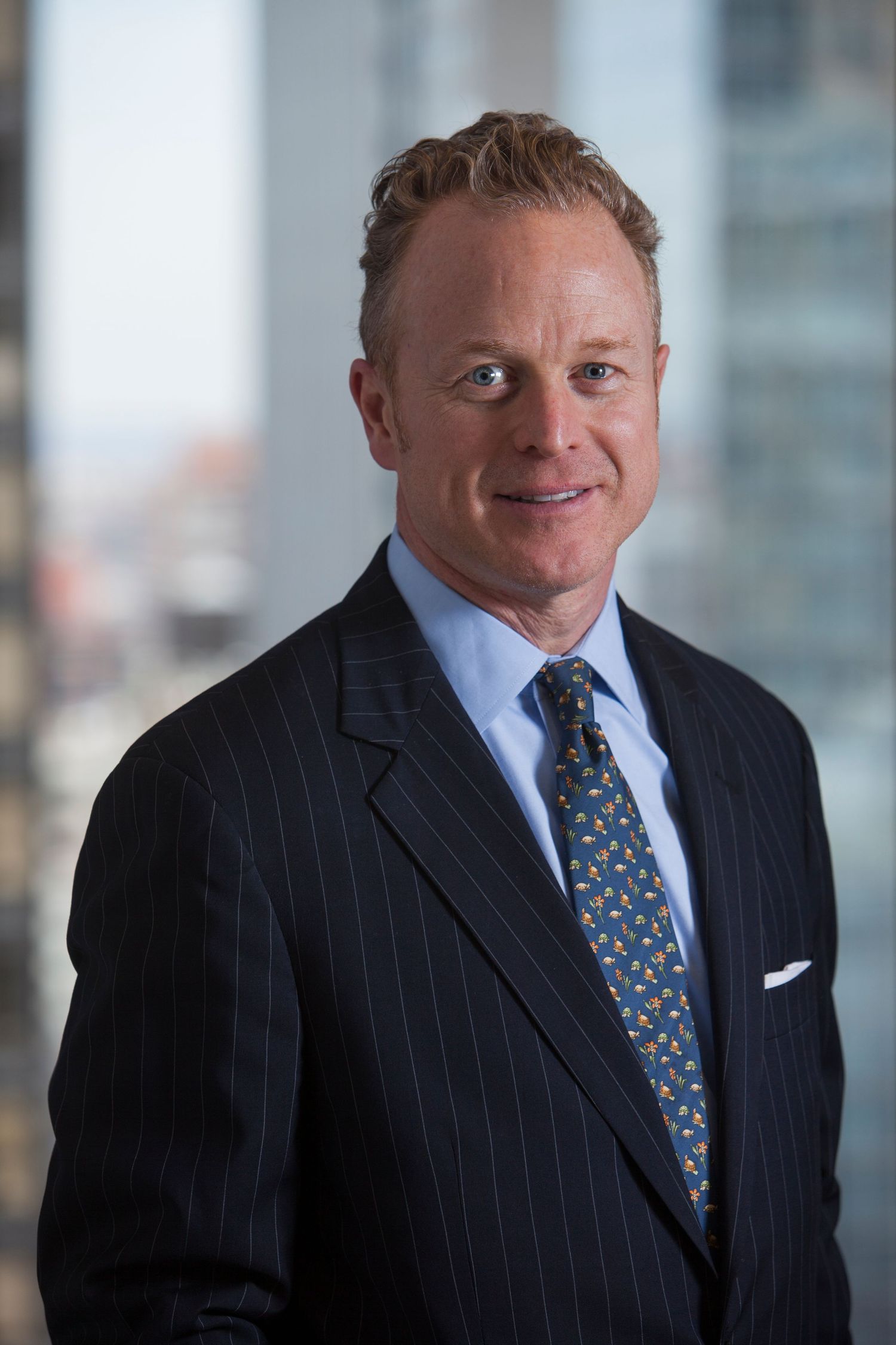 Confident businessman in pinstripe suit and patterned tie posing in a high-rise office.