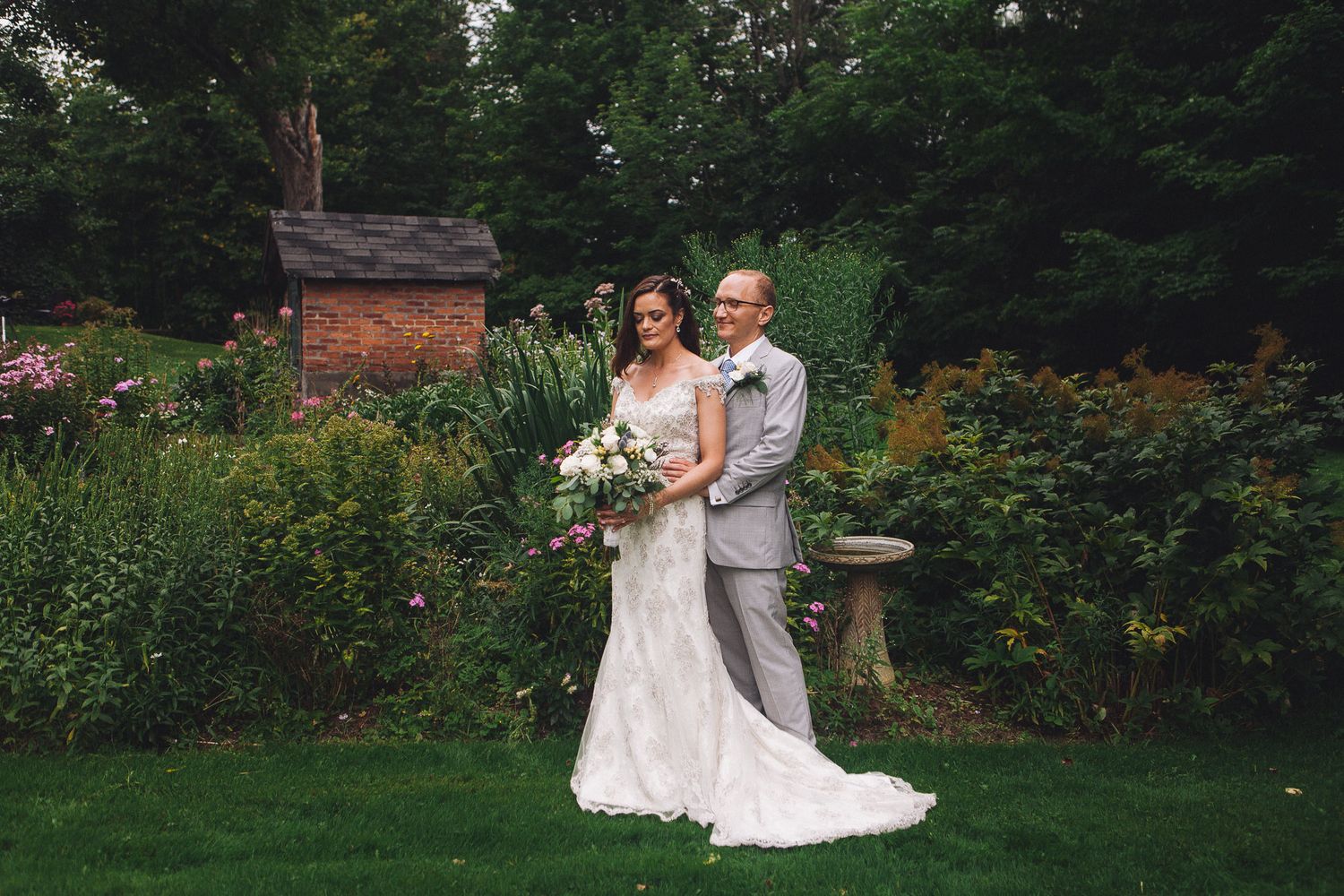 Bride holding bouquet with groom in grey suit in lush garden wedding portrait.