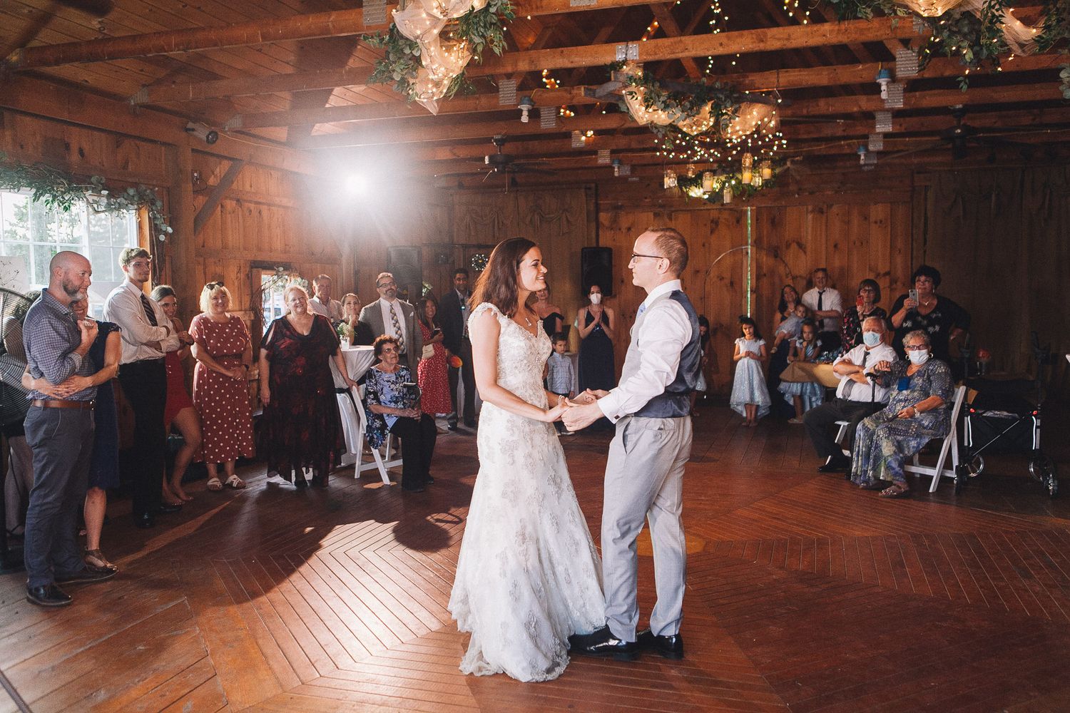 Bride and groom share their first dance in a rustic barn wedding venue with guests watching.