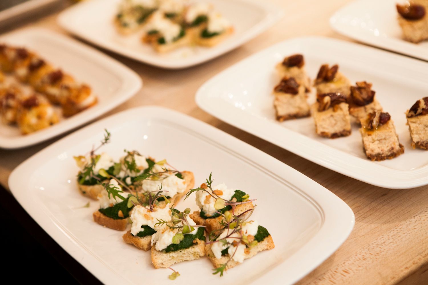 Elegant appetizer canapés with cream cheese and herbs on toasted bread on white plates.
