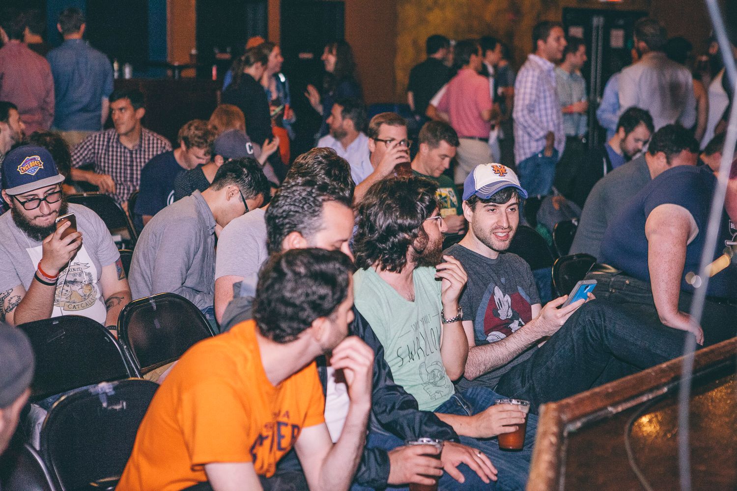 Crowd of young people socializing and using phones at an indoor event venue.