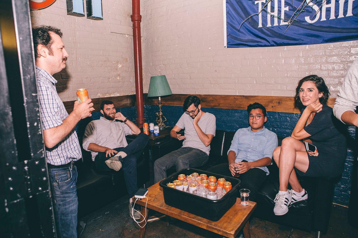 Group of friends relaxing on couches at a casual indoor gathering with drinks and snacks.