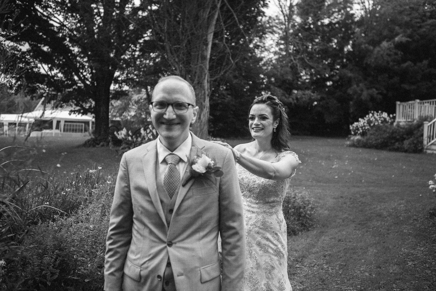 Bride surprising groom from behind in black and white outdoor wedding garden photo.