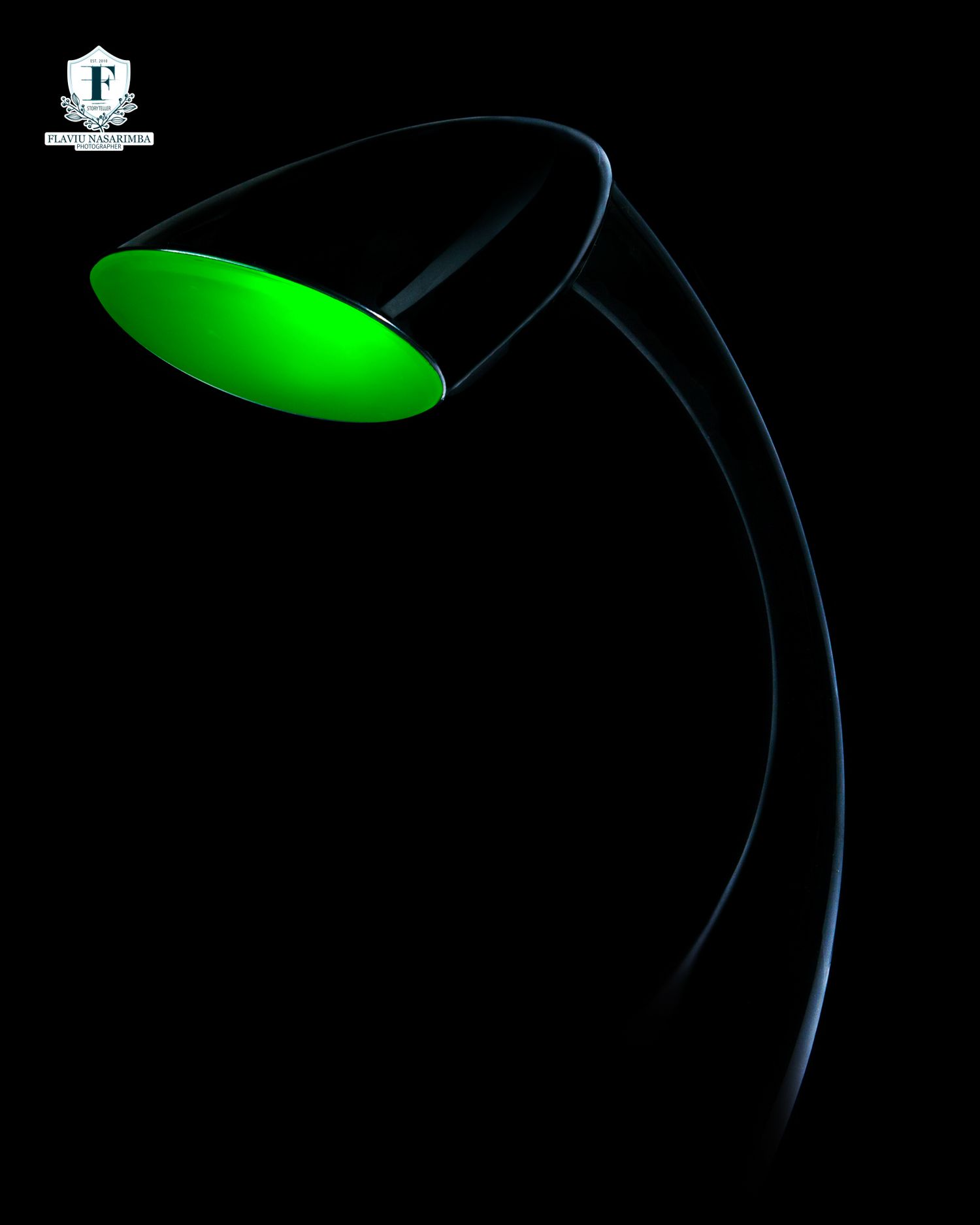 Artistic dark photo of a modern green illuminated desk lamp against a black background.
