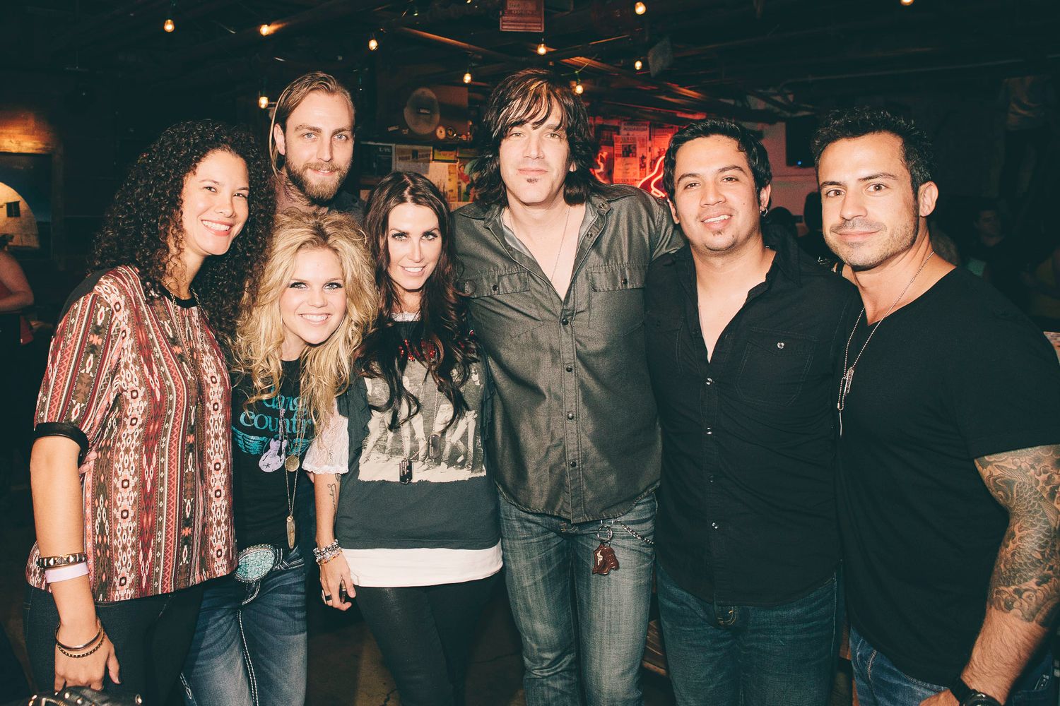 Group of seven people posing together smiling at an indoor music venue event.