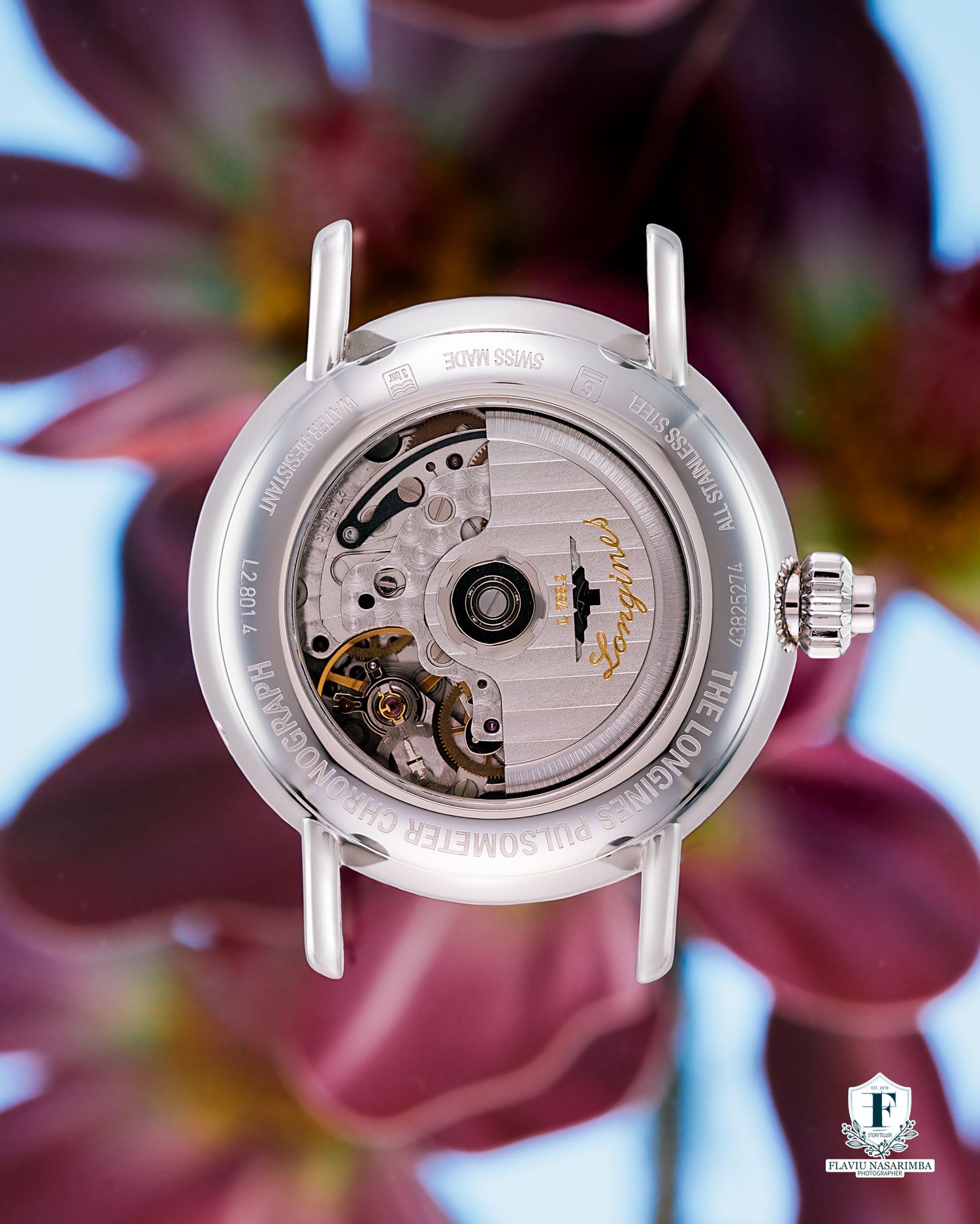 Longines watch with visible automatic movement through caseback, surrounded by vibrant red flowers.