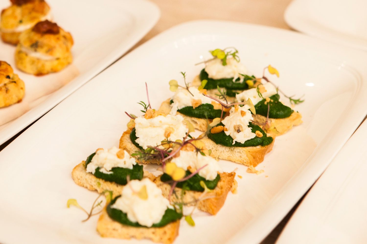 Crostini appetizers topped with sauteed spinach, ricotta, and fresh herbs on a white rectangular plate.