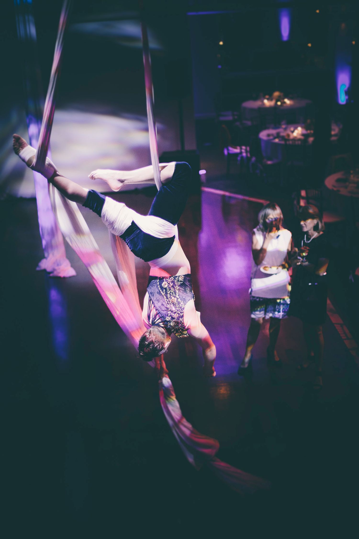 Acrobat performing aerial silks upside down at an indoor event with guests watching in the background.