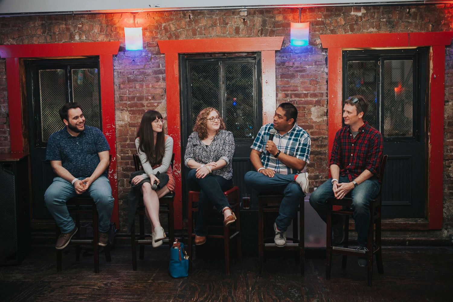 Five people seated on stools laughing together at an indoor panel discussion event.