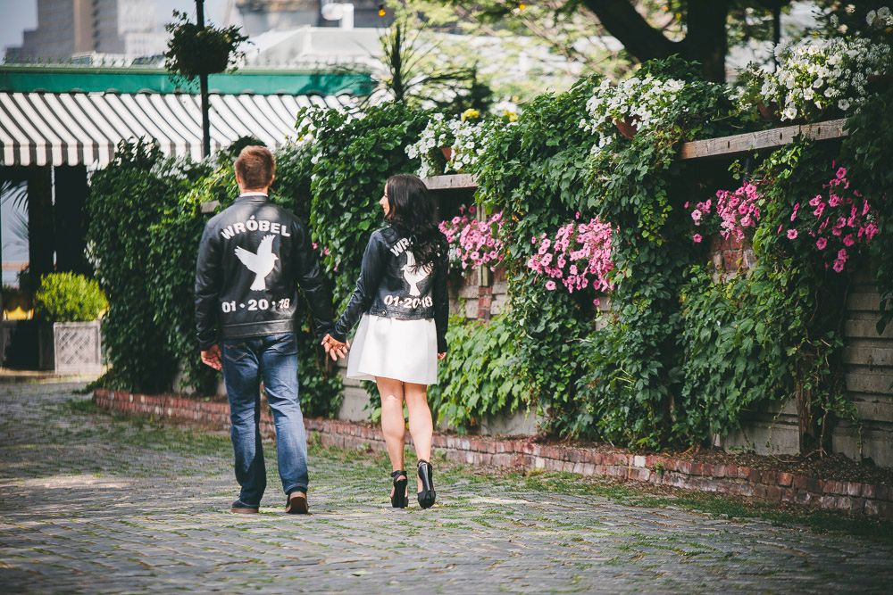 Couple walking hand in hand wearing matching custom black jackets on a cobblestone street.