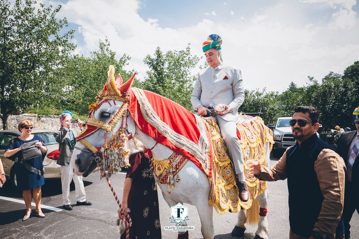 Groom in white sherwani rides decorated white horse during traditional Indian baraat wedding procession.