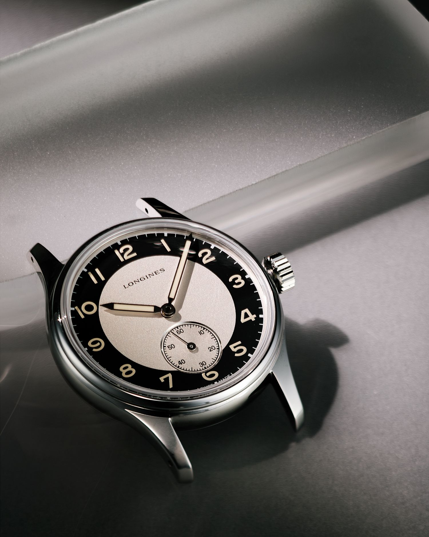 Elegant Longines vintage-style watch with two-tone dial and Arabic numerals on gray surface.