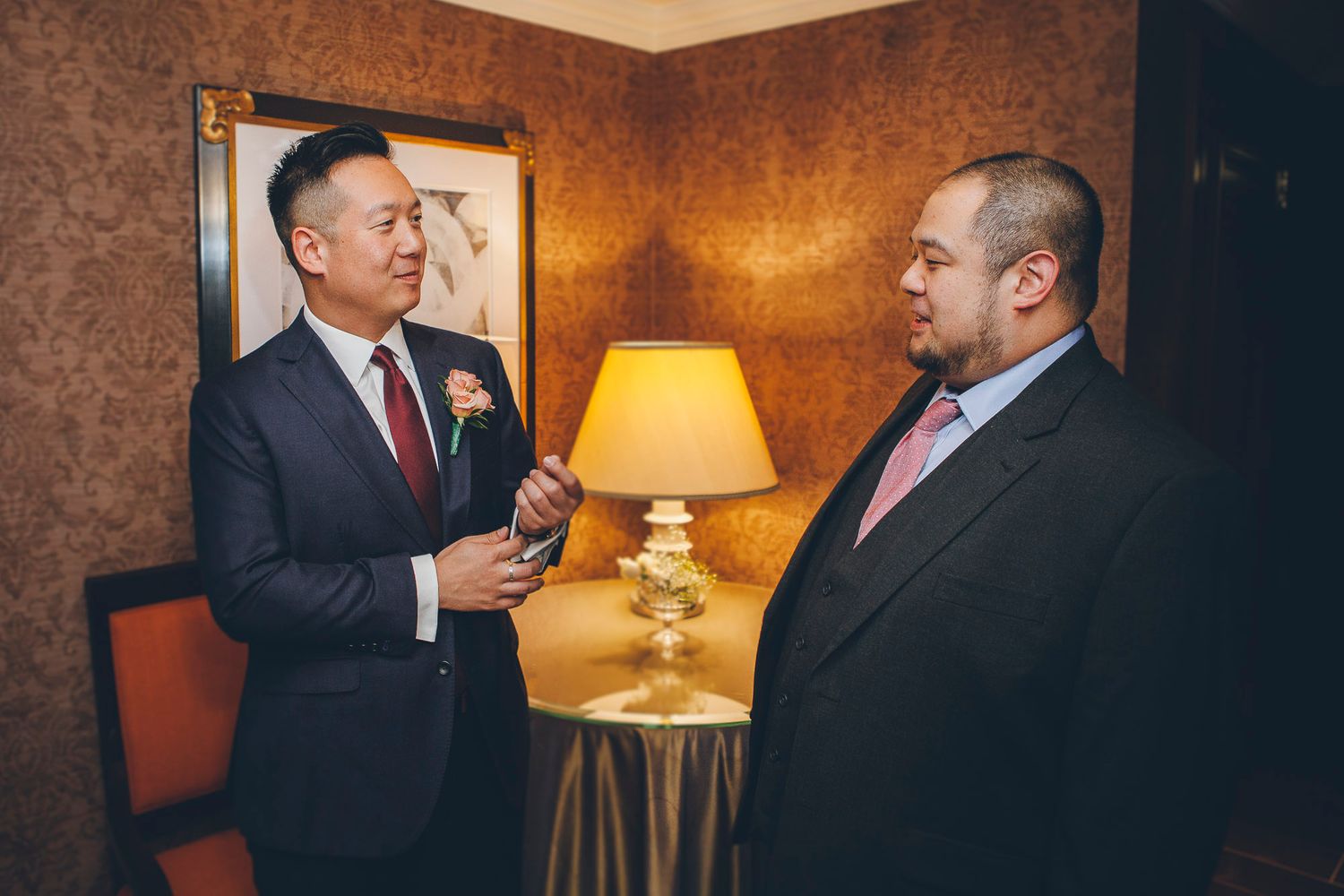 Groom in navy suit with floral boutonniere having a conversation with a guest before the wedding.