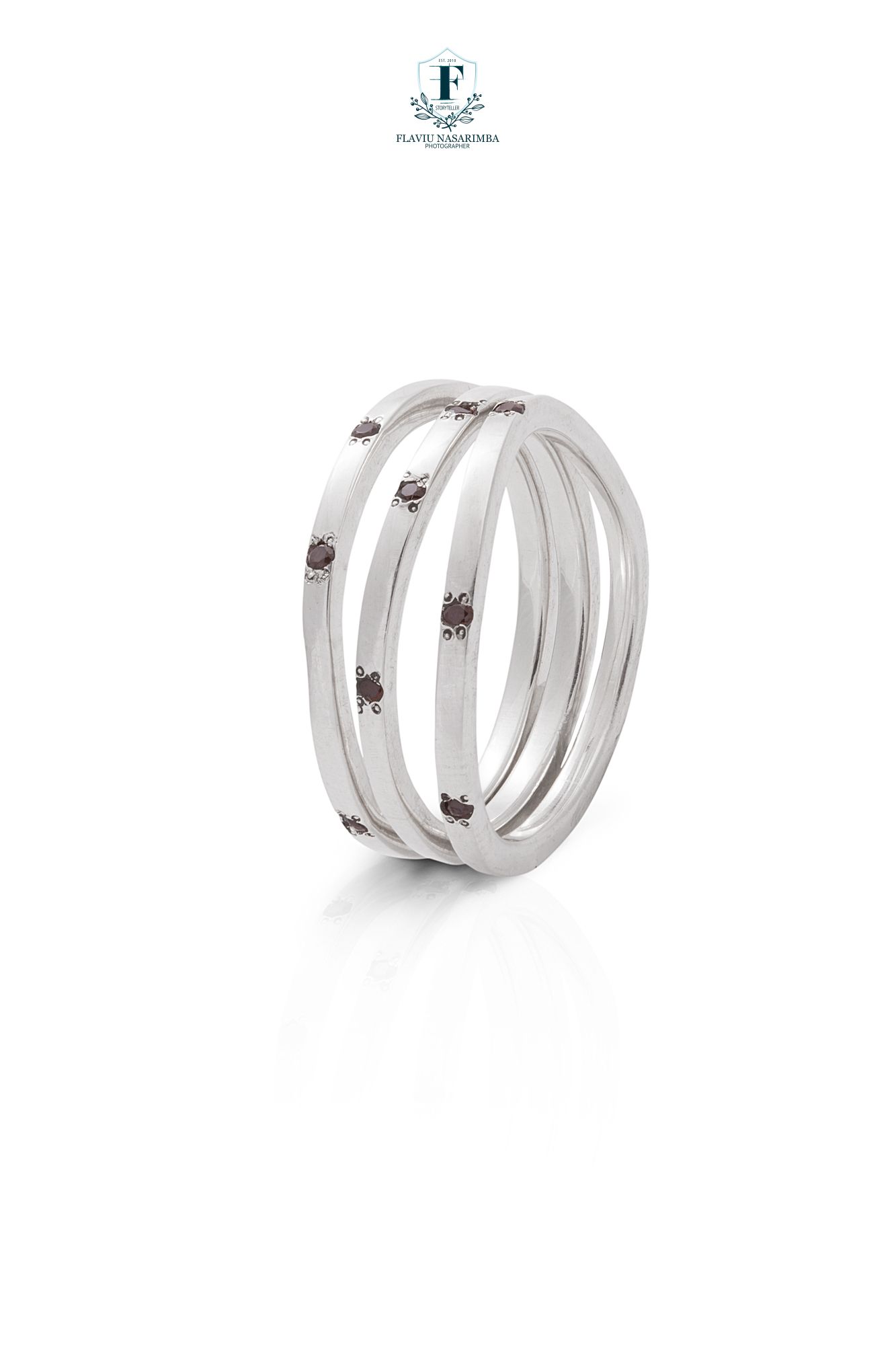 Triple-band silver ring with small dark gemstone accents on clean white background.
