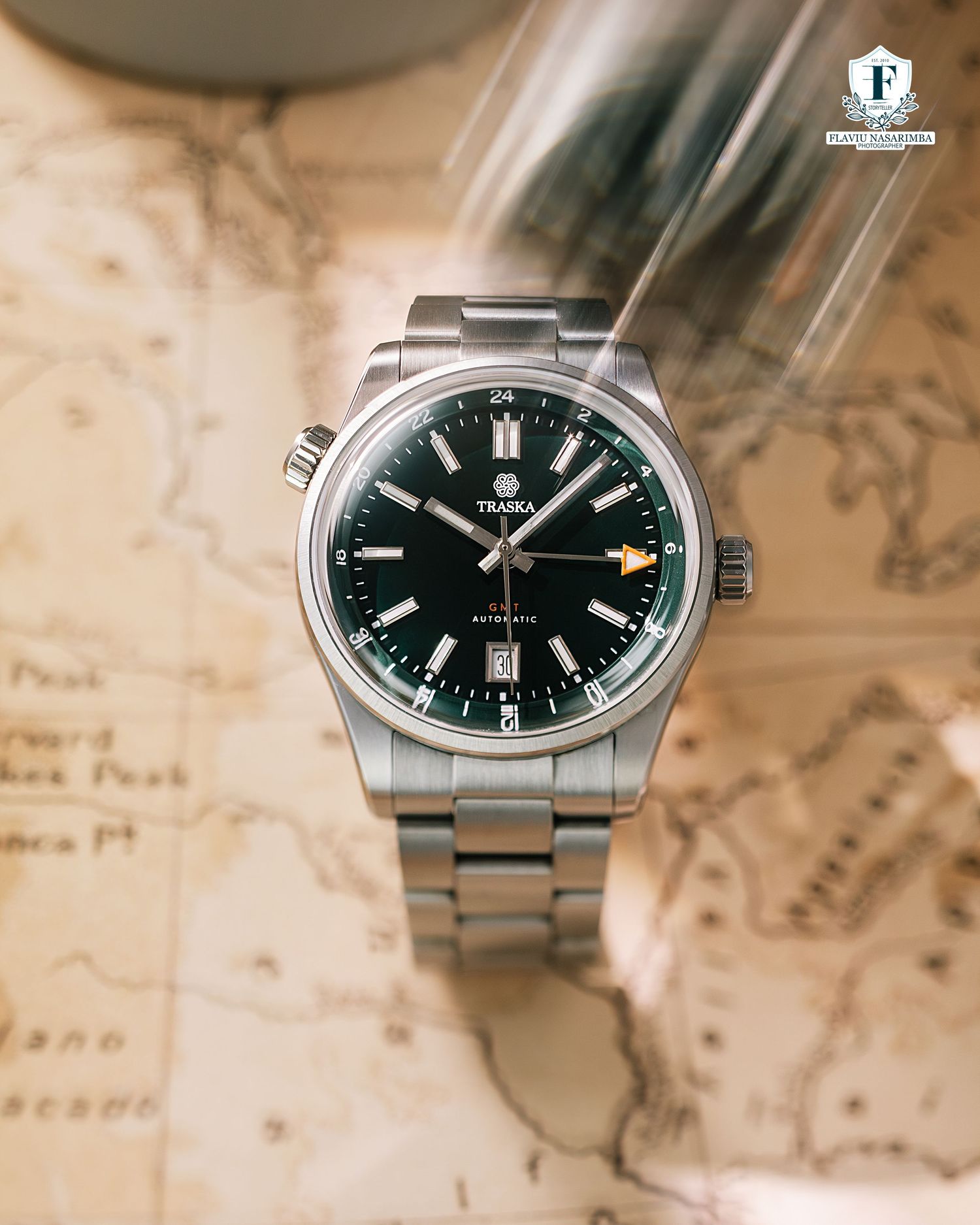 Traska automatic GMT watch with green dial on stainless steel bracelet over a vintage map.