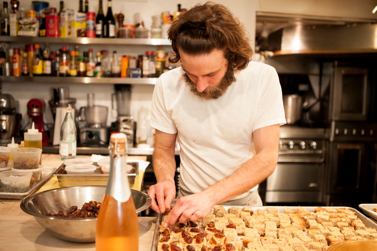 Bearded chef preparing bite-sized appetizers on a baking tray in a professional kitchen.