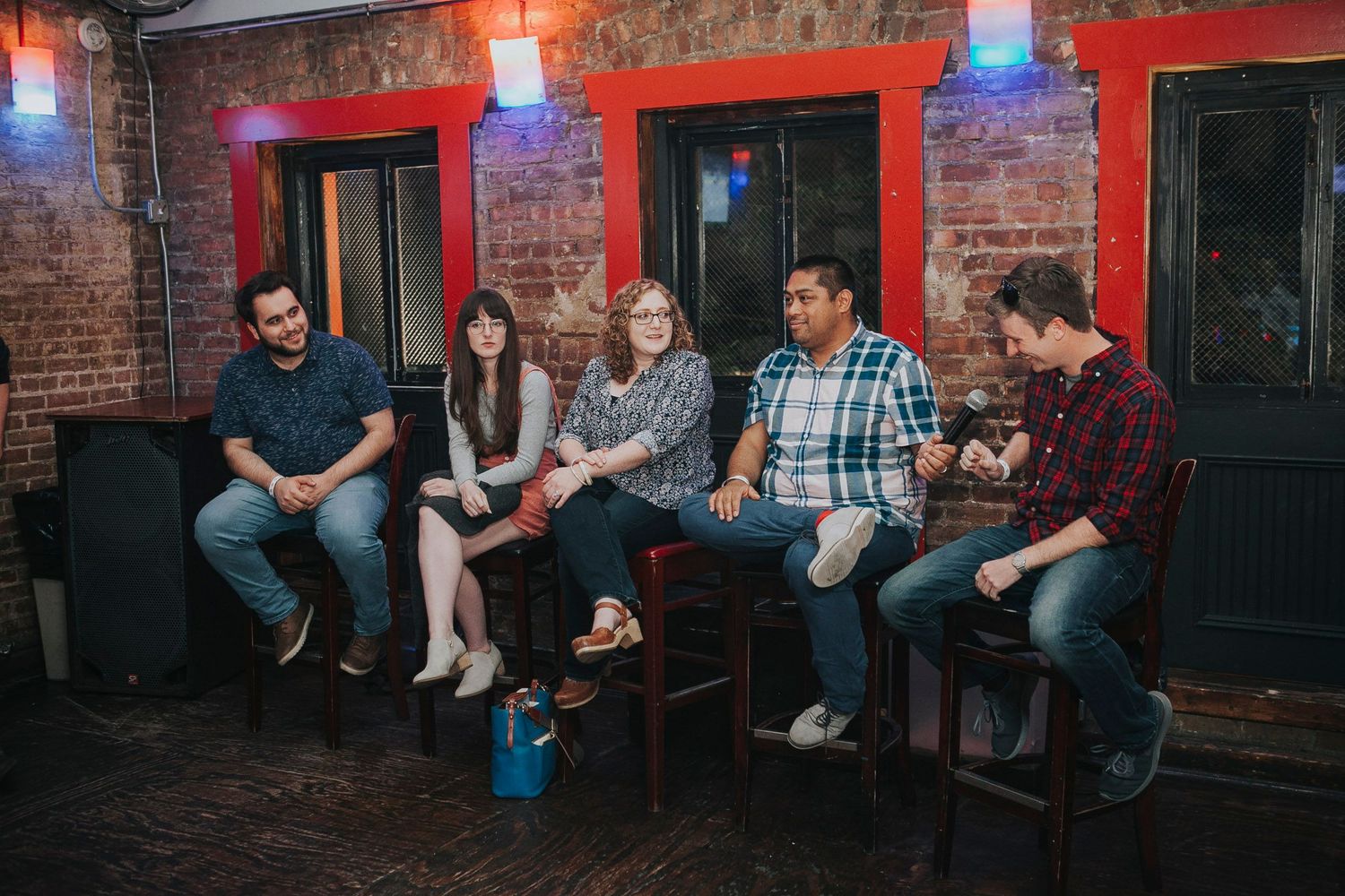 Five people seated on stools in a relaxed panel discussion in a brick-walled bar.