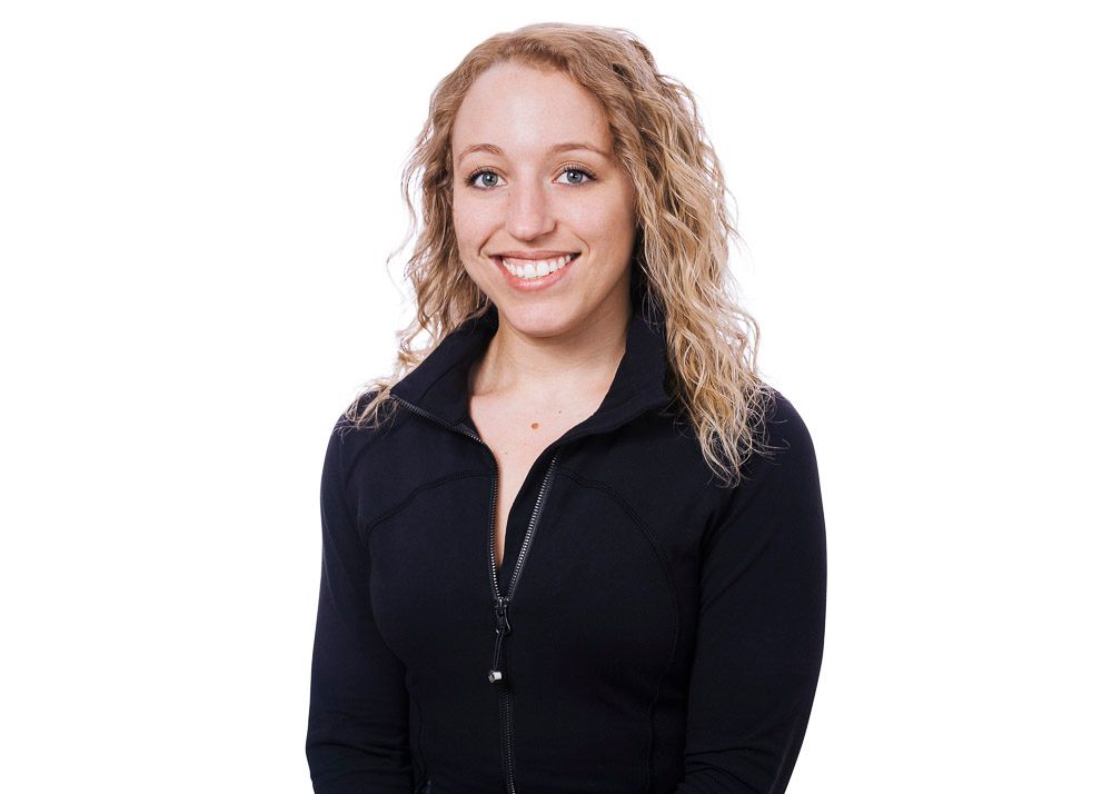 Professional headshot of a smiling woman with curly blonde hair wearing a black zip-up jacket.