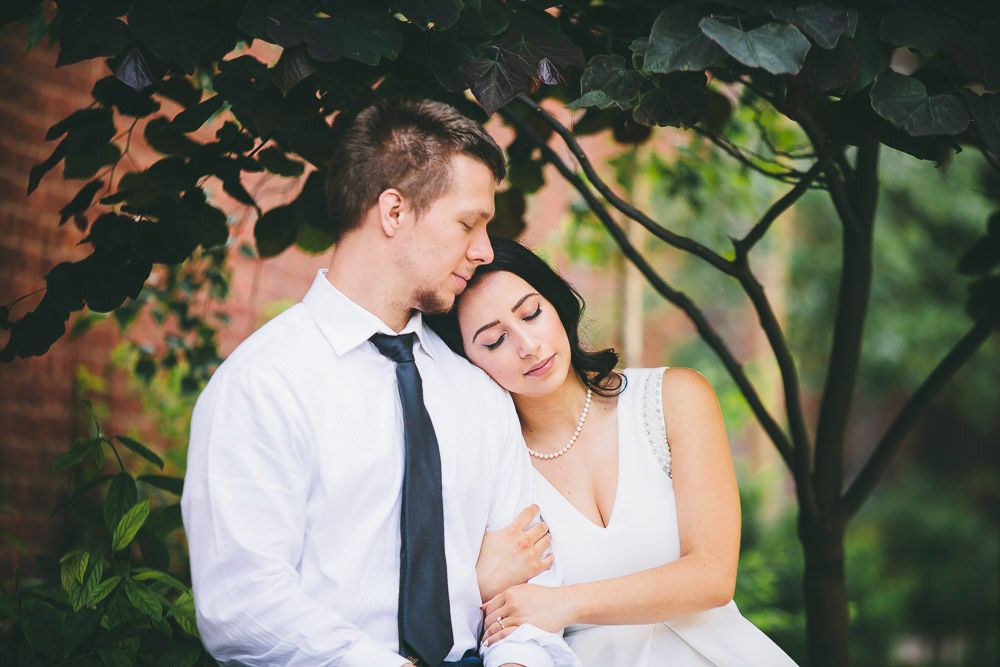 Romantic couple embracing tenderly under lush green trees in a garden setting.