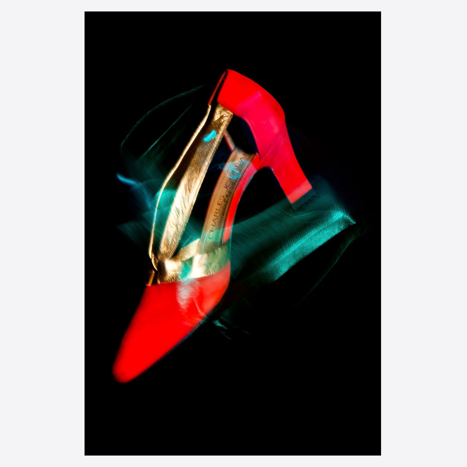 A vibrant red high-heel shoe with gold accents glows against a black background with teal light streaks.