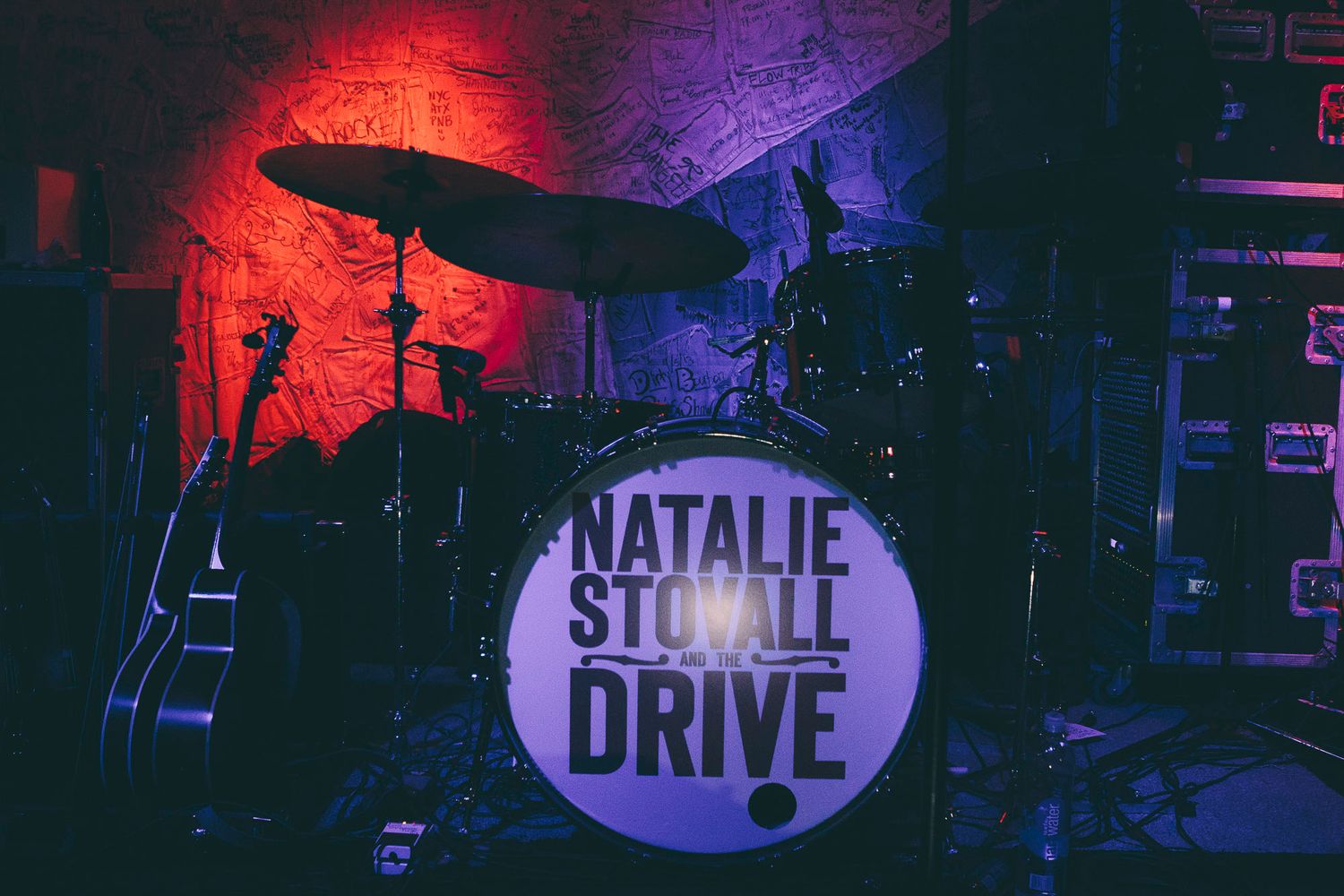 Natalie Stovall Drive band drum kit on stage under dramatic red and purple stage lighting.