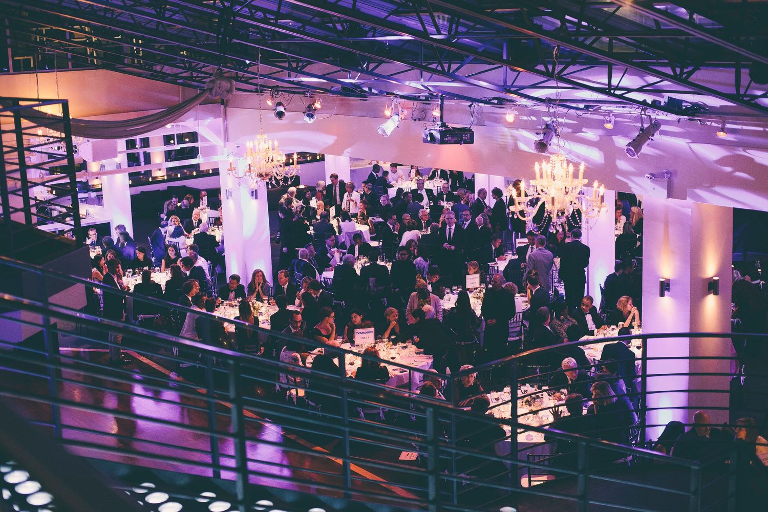 Aerial view of an elegant gala event with guests dining in a large venue with purple uplighting.