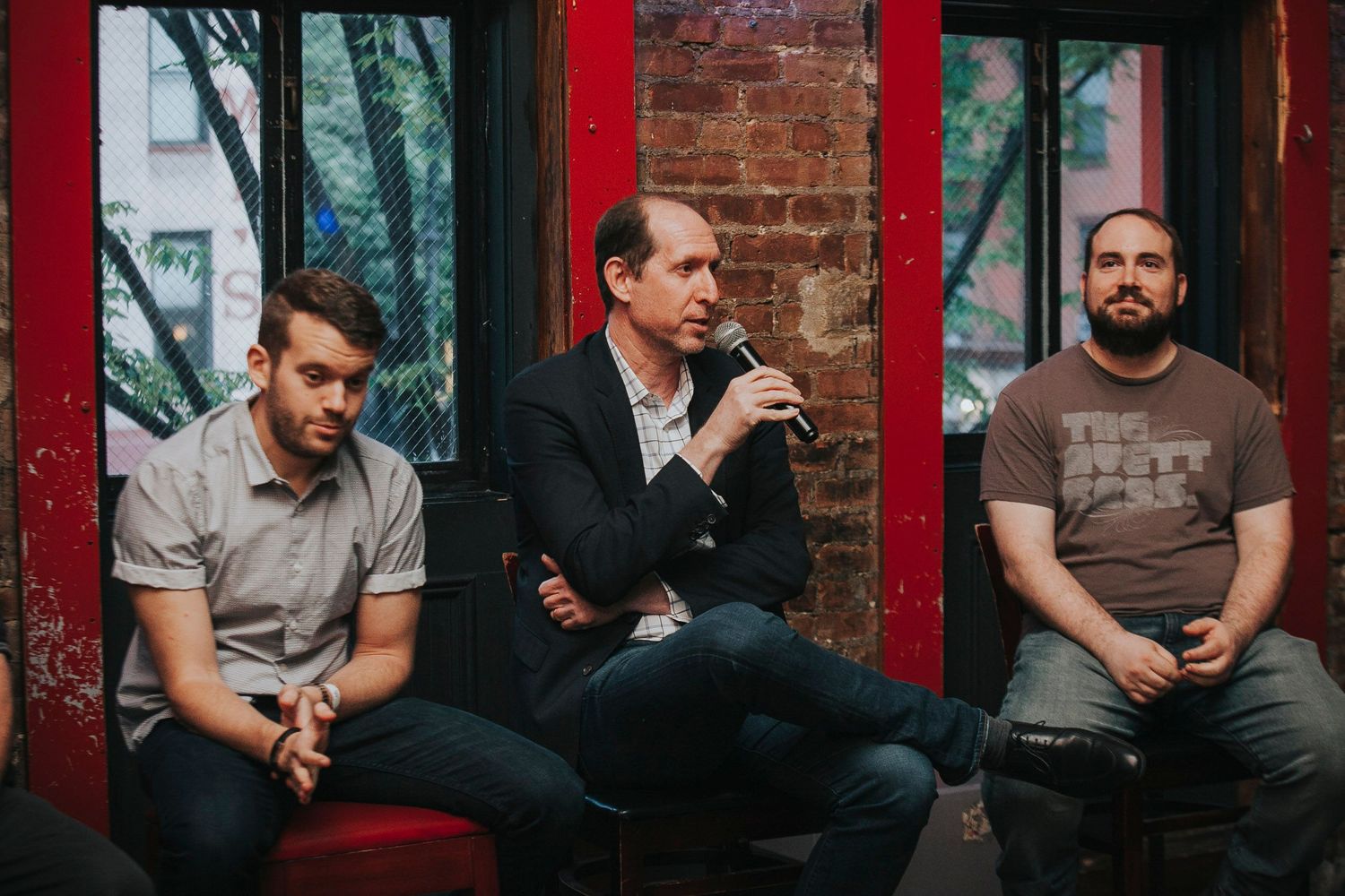 Three men seated in front of a brick wall during an indoor panel discussion event.