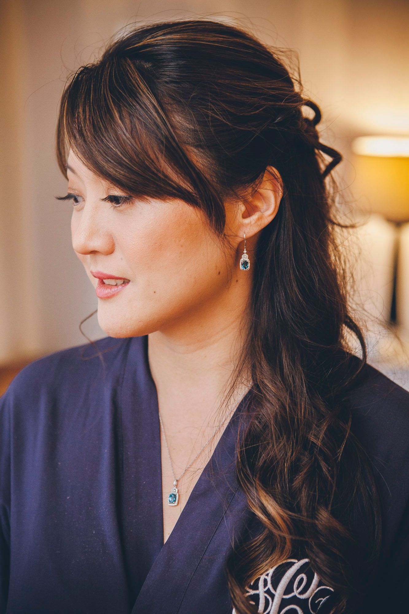 Beautiful Asian bridesmaid with half-up hairstyle wearing drop earrings and navy monogram robe.