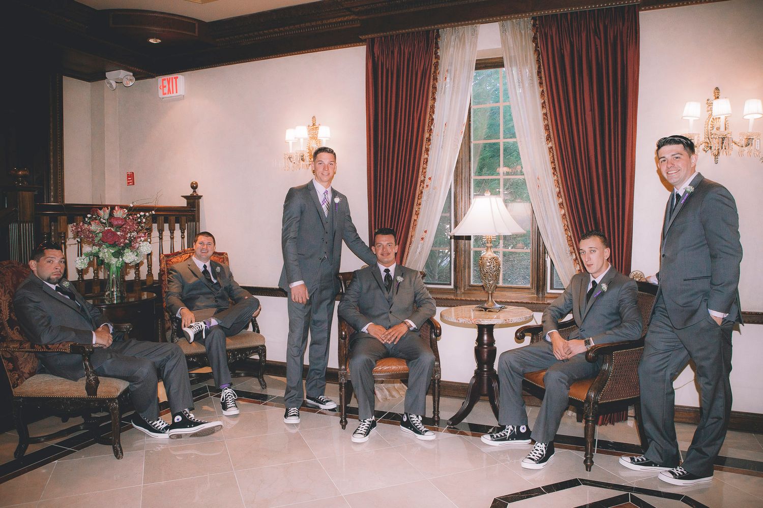 Groomsmen in matching gray suits posing casually in an elegant hotel lobby before a wedding ceremony.