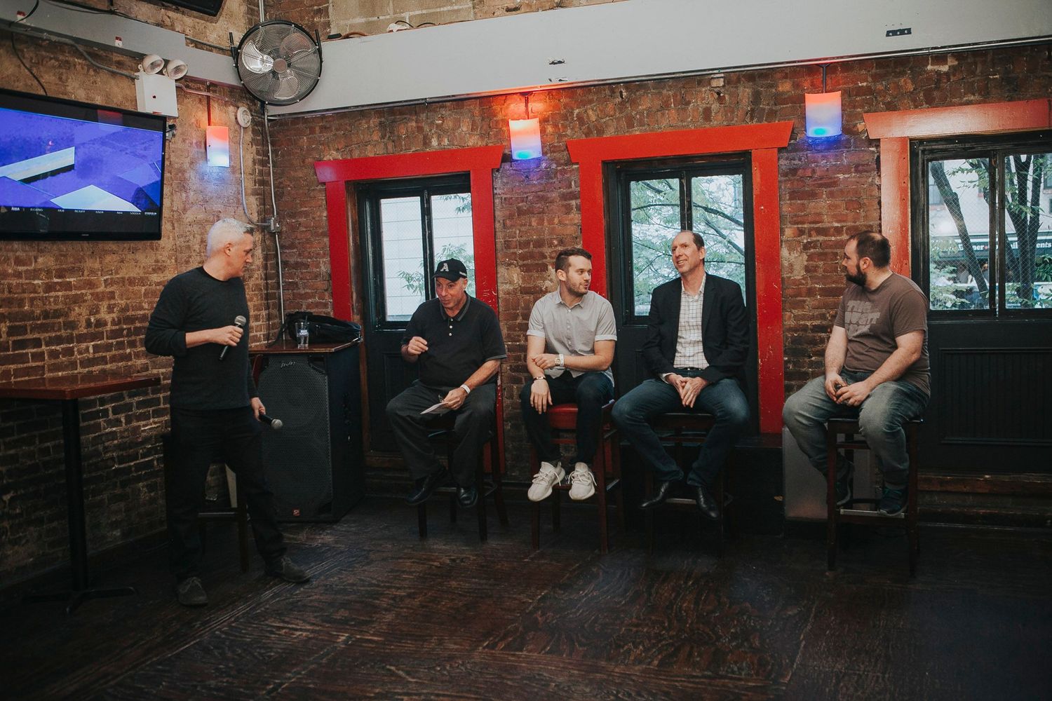 Five men participate in a panel discussion at a brick-walled venue.
