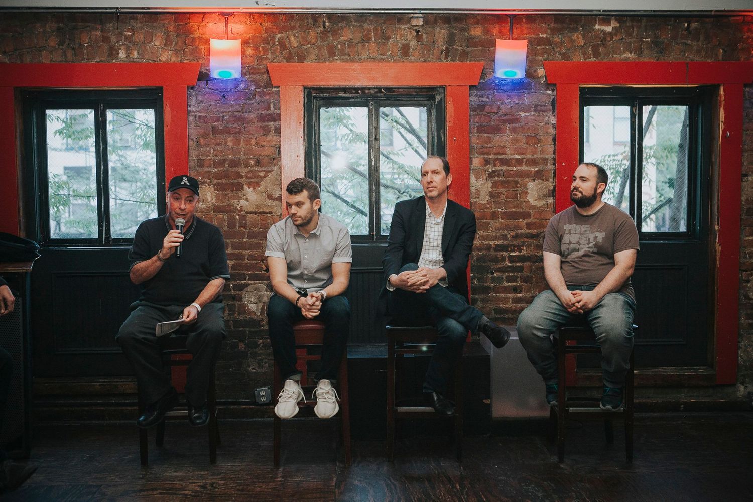 Four men sit on chairs against brick wall during a panel discussion.