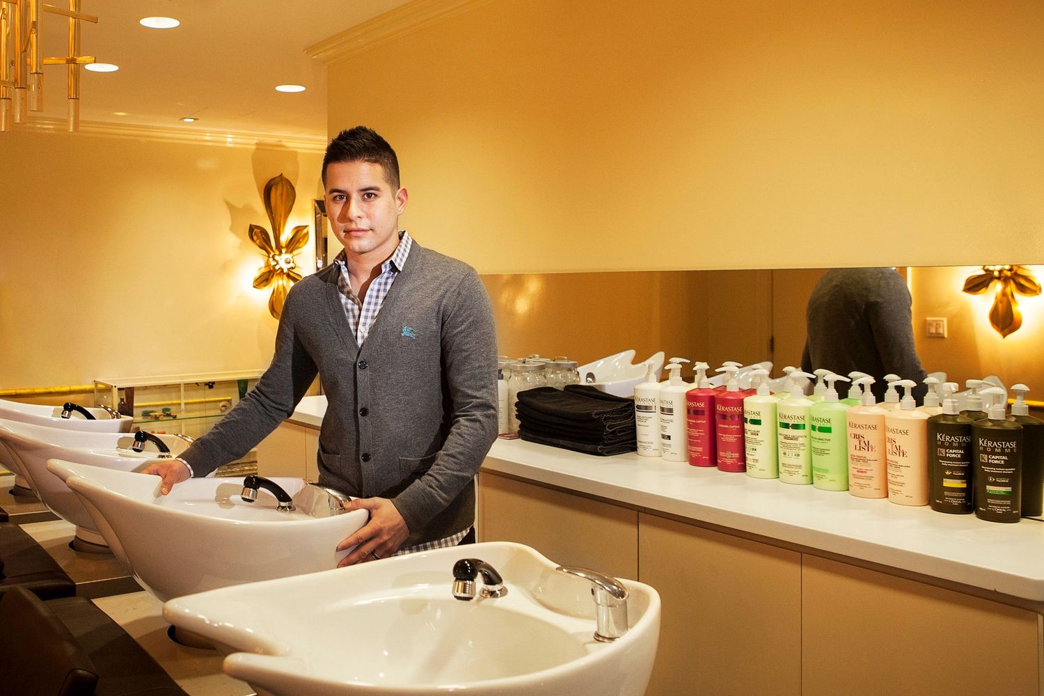 Young man standing at a hair salon wash station with product bottles on the counter.
