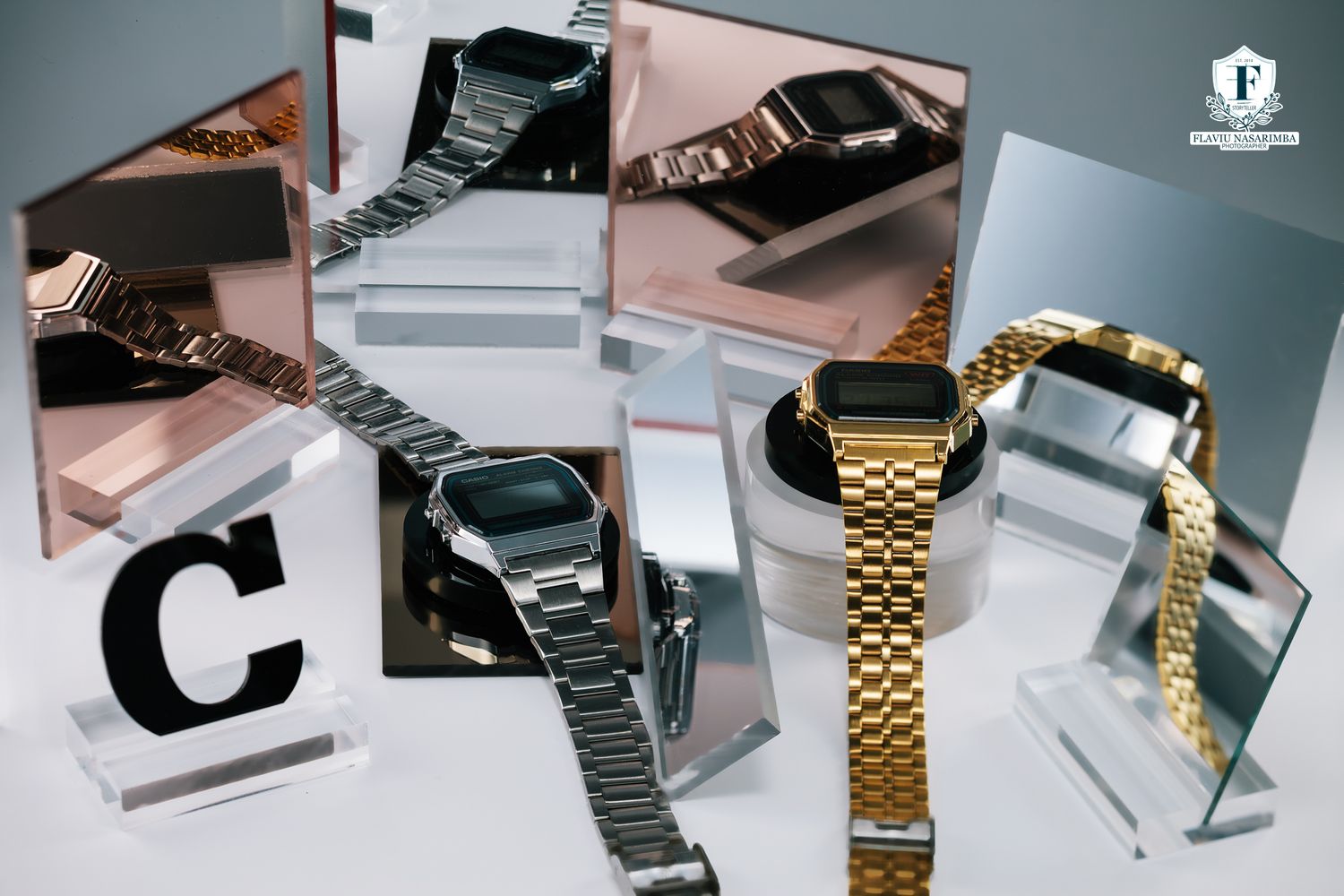 Casio digital watches displayed with gold and silver metal bracelets on mirrored acrylic stands.
