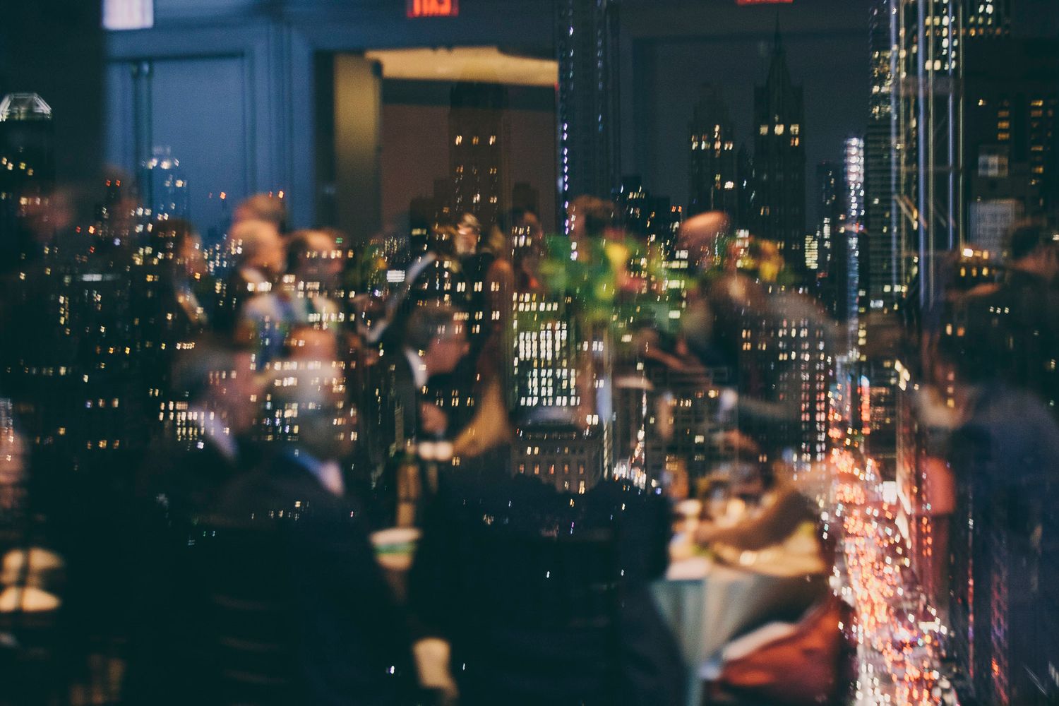 Blurred cityscape view through window with wedding reception guests dining at night.